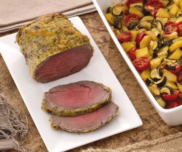 Roast beef with citrus fruits with a tray of potatoes, zucchini, and cherry tomatoes